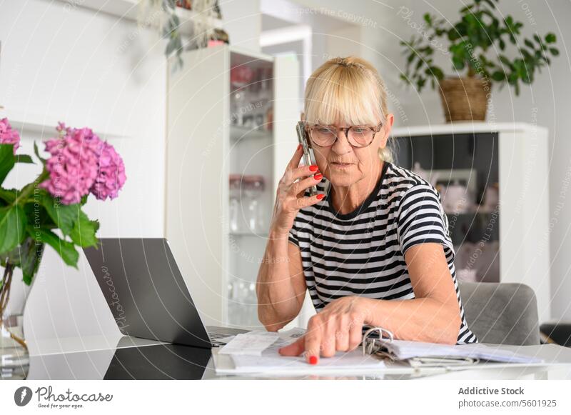 Besorgte alte Frau liest Zeitungen und führt ein Telefongespräch im heimischen Wohnzimmer Textfreiraum Buchhaltung gealtert Banking Rechnung Haushaltsplan