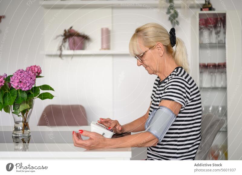 Ältere Frau misst Blutdruck zu Hause prüfen Senior messen Druck heimwärts Routine Tisch geduldig Fokus untersuchen reif achtsam sitzen täglich Konzentration