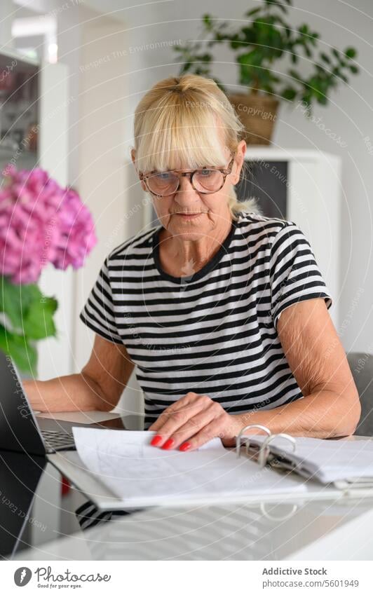 Ältere Frau prüft Dokumente und schreibt Notizen Papier lesen Papierkram Schriftstück heimwärts prüfen Tisch modern reif lässig sitzen Konzentration klug Arbeit