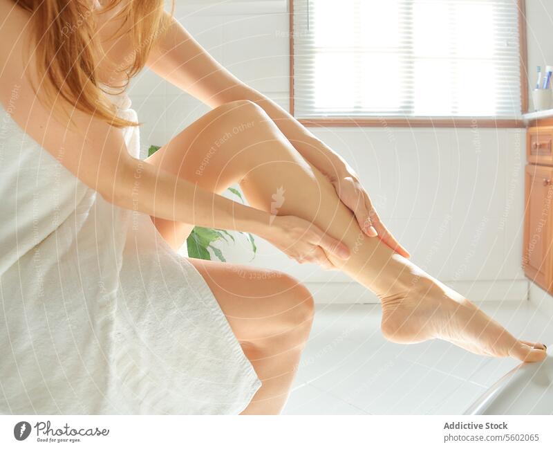 Wellness- und Hautpflegekonzept. Junge Frau massiert ihre Beine nach der Enthaarung im Badezimmer. Rasieren Körper heimwärts Mädchen Spa benutzend danach depil
