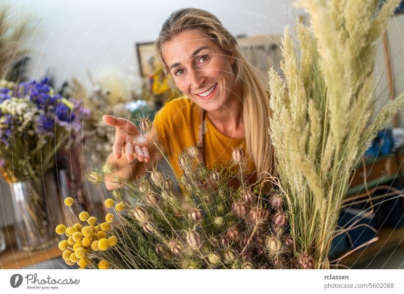 Blumenhändlerin präsentiert eine Auswahl an Trockenblumen in ihrem Geschäft Blumenladen präsentierend Floristik botanisch Dekoration & Verzierung Gesteck