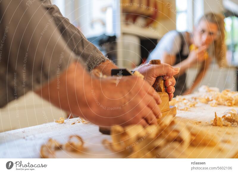 Ein Auszubildender beobachtet interessiert, wie ein Tischler in einer Werkstatt Holz hobelt Schreinerei Kapselgehörschützer Kunsthandwerker Hobelbank Azubi