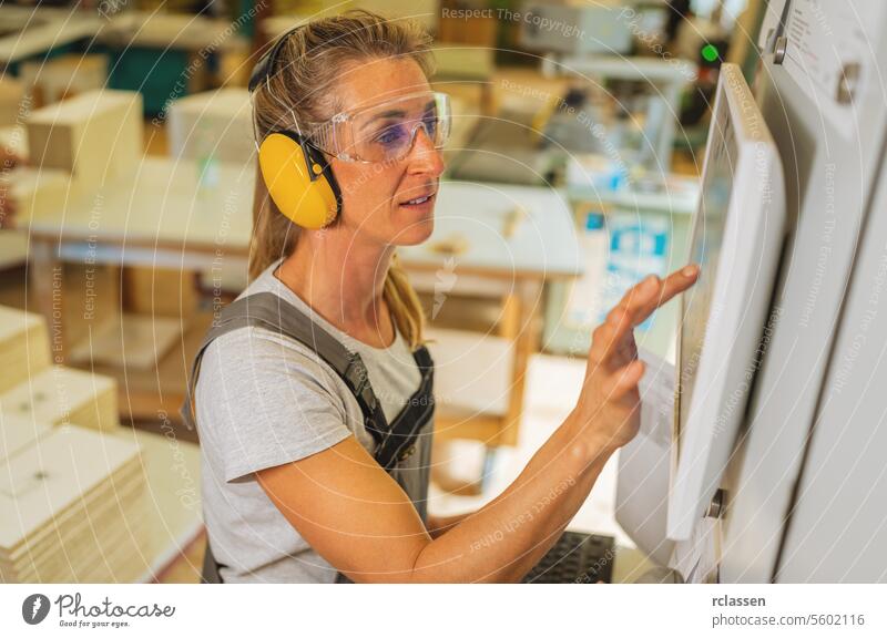 Frau mit Gehörschutz bei der Bedienung eines Touchscreens an einer Schneidemaschine in einer Tischlerei professioneller Handwerker Kapselgehörschützer