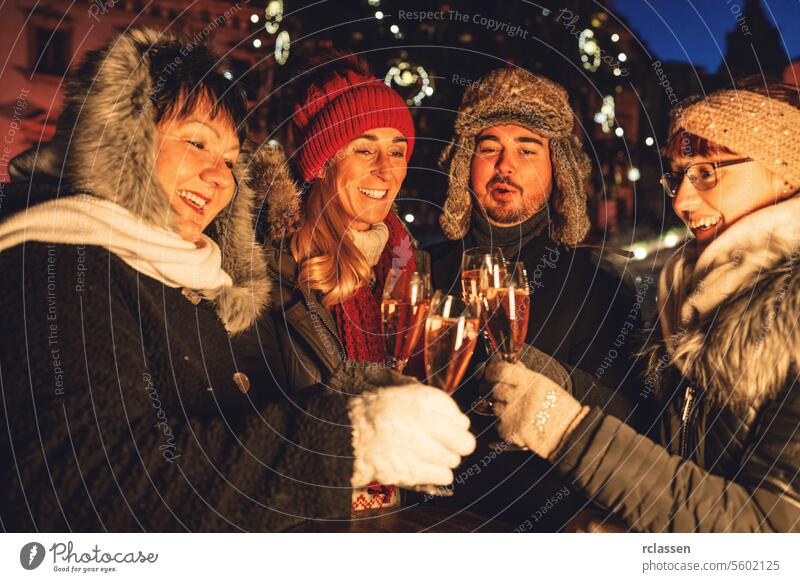 Eine Gruppe von Freunden stößt mit Champagner in einer festlichen Nacht auf einem Weihnachtsmarkt an Menschengruppe Neujahr Paar Röstung Winter Abend Brille