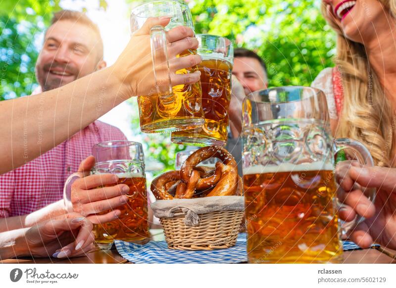 Freunde in Tracht, Dirndl und Lederhosen, die am Tisch sitzen, Bier trinken und Brezeln essen im Biergarten oder auf dem Oktoberfest in Bayern, Deutschland