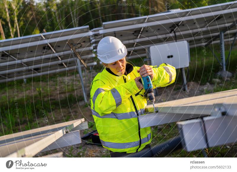 Weiblicher Techniker mit einem Akkubohrer auf Solarpanel Struktur in einem Feld. Alternative Energie ökologisches Konzept Bild. Technik & Technologie Pflanze
