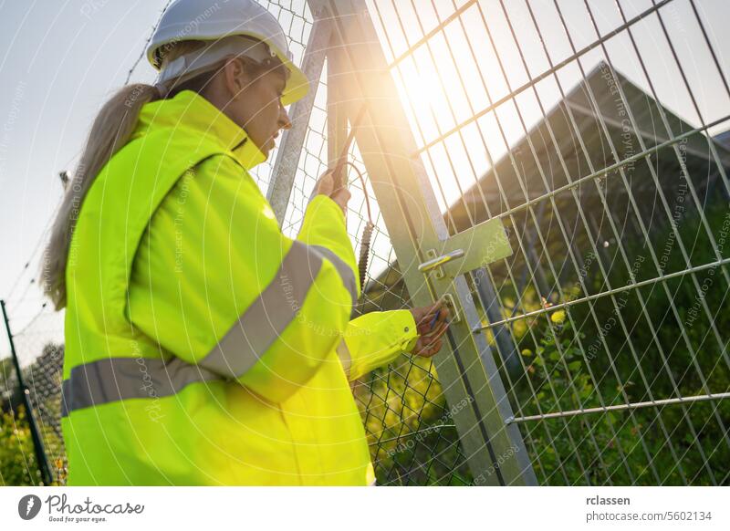 Weiblicher Techniker verriegelt Tor an Solaranlage bei Sonnenuntergang. Alternative Energie ökologisches Konzept Bild. Technik & Technologie Pflanze Industrie