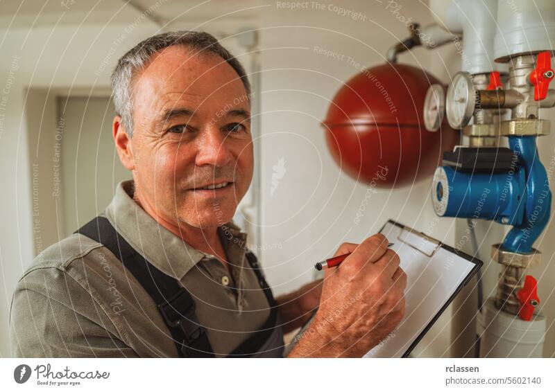 Ingenieur, der die Heizungsrohre im Gaskesselraum kontrolliert, mit Checkliste auf einer Zwischenablage. Gasheizung Ersatz Verpflichtung Konzept Bild Wassertank