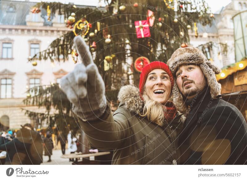 Überrascht Frau zeigt mit ihrer Hand, um ihren Freund etwas auf dem Weihnachtsmarkt im Winter in Deutschland zu zeigen zeigende Hand Neujahr trinken Weihnachten