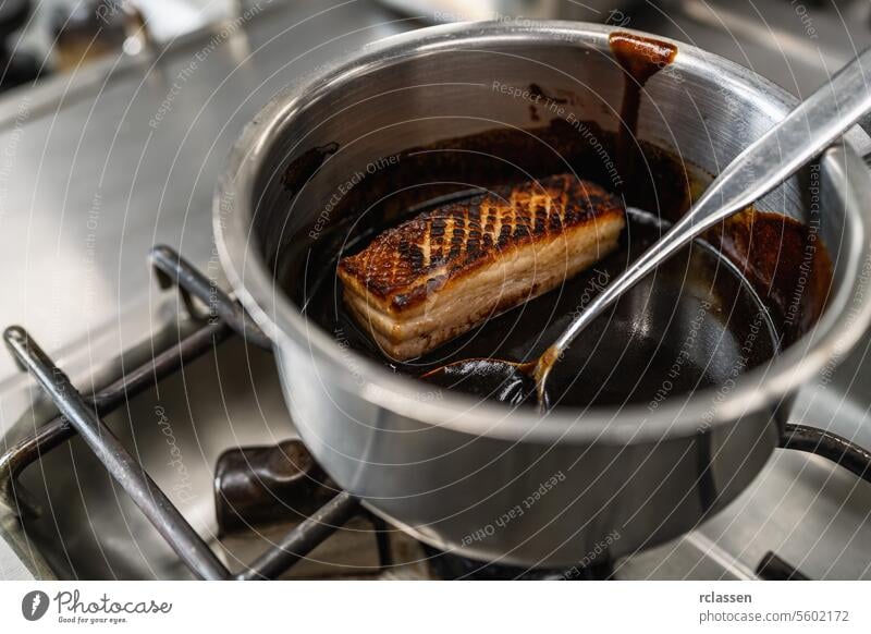 Knusprig gebratenes Schweinefleisch glasiert mit brauner Soße in einem Topf in einer professionellen Küche in einem Restaurant. Luxus-Hotel Kochen Konzept Bild.