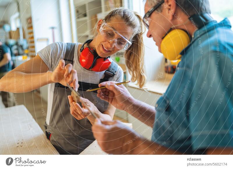 Schreinerlehrling und Lehrling messen ein Holzstück in einer gut beleuchteten Werkstatt aus professioneller Handwerker Hobelbank Möbelindustrie Arbeiter