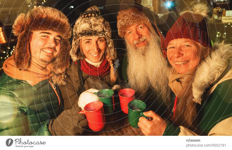 Eine glückliche Familie stößt mit Glühwein und heißer Schokolade auf einem Weihnachtsmarkt an und trägt Wintermützen Tourist Menschengruppe Freunde Großeltern