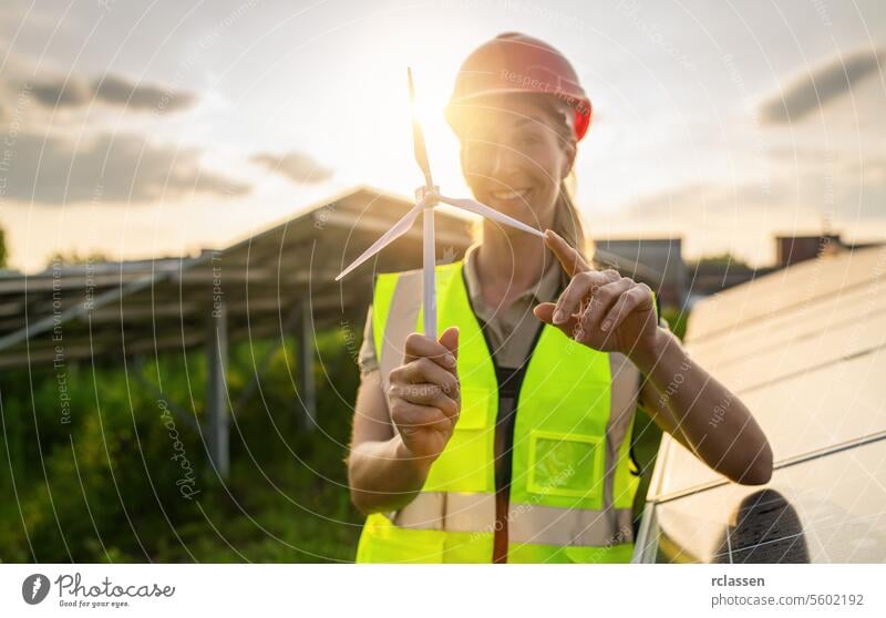 Lächelnde Ingenieurin hält ein Windturbinenmodell in einem Solarpark. Alternative Energie ökologisches Konzept Bild. Photovoltaik Technik & Technologie
