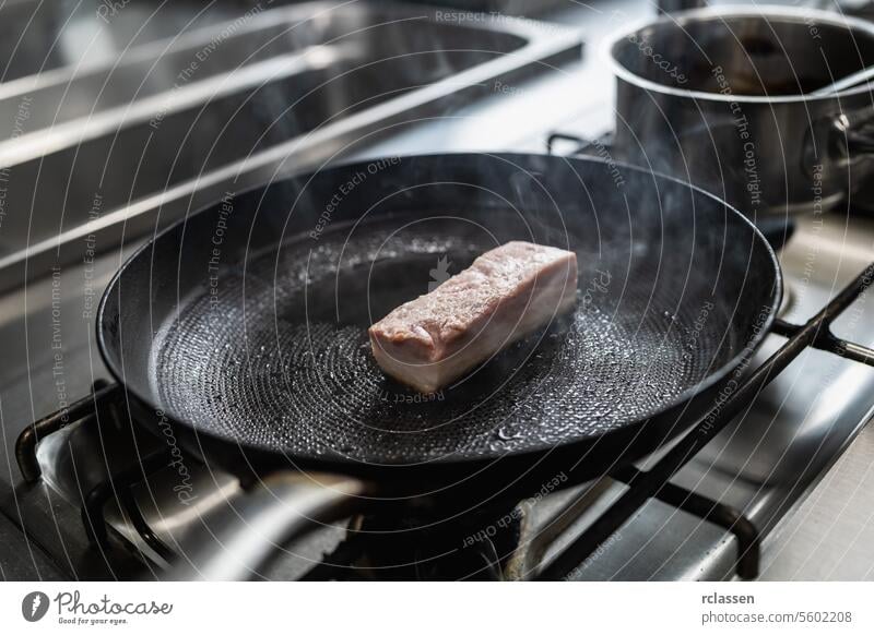 Roher Schweinebraten in heißer Pfanne mit Öl auf einem Gasherd in einer professionellen Küche in einem Restaurant. Luxus-Hotel Kochen Konzept Bild. roh Kruste