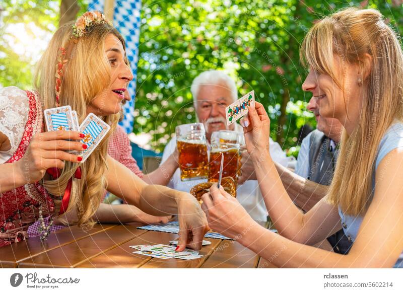 Freunde in Tracht spielen das traditionelle Kartenspiel Schafkopf in einem deutschen Biergarten oder auf einem Oktoberfest Glücksspiel Spielen Blockwart