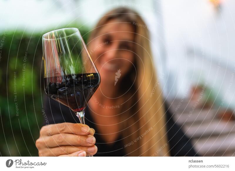 Frau, die mit einem Glas Rotwein anstößt, unscharfer Hintergrund Restaurant Abendessen Gläserklirren Italien Sommerzeit Röstung verschwommener Hintergrund