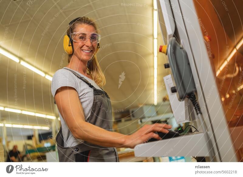 Frau, die einen Computer an einer Schneidemaschine in einer Tischlerwerkstatt benutzt erfahrener Handwerker Kapselgehörschützer Schutzbrille