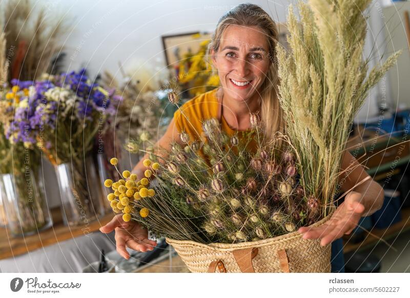 Glückliche Floristin mit einem Korb voller Trockenblumen in einem Blumenladen Blumenhändler Frau Lächeln natürlich Dekoration & Verzierung Kunstgewerbler