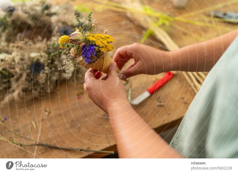 Hände, die einen kleinen Strauß bunter Trockenblumen in einem Kegel auf einem Holztisch binden Messer Werkstatt Basteln Blumenstrauß farbenfroh Zapfen Floristik