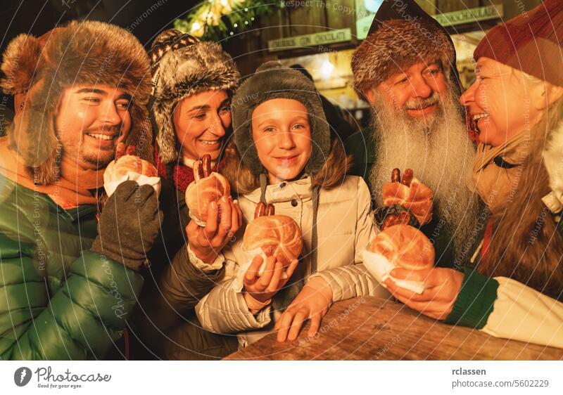 Familie genießt Würstchen auf einem Weihnachtsmarkt, lächelnd zusammen mit Wintermützen Frohe Weihnachten Handschuhe traditionell Glühwein Deutsch