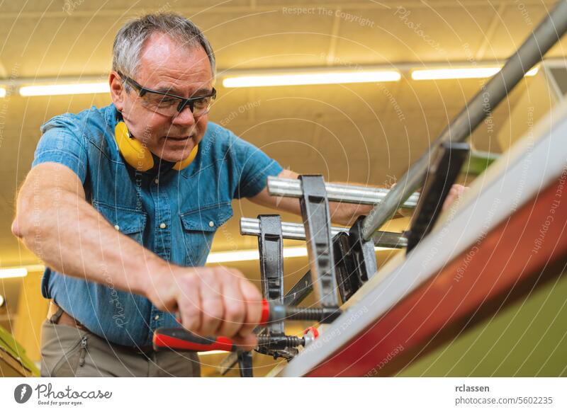 Fokussierter Tischler mit Gehörschutz bei der Arbeit mit Zangen und Holz in einer Werkstatt professionell Kunsthandwerker Hobelbank Möbelindustrie Arbeiter