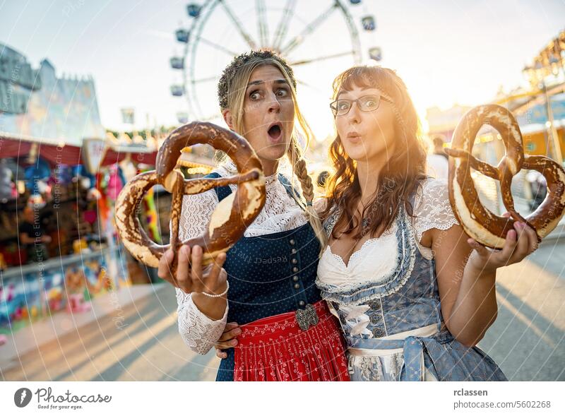 Zwei glückliche Freundinnen zusammen auf einer bayerischen Kirmes oder einem Oktoberfest oder in Tracht oder Dirndl mit Brezn oder Brezen in Deutschland Frau
