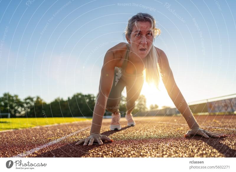 Intensive weibliche Athletin an der Startlinie auf der Rennstrecke bei Sonnenuntergang Sportlerin intensiv Tatkraft Sportbekleidung Fitness laufbereit Sprinter