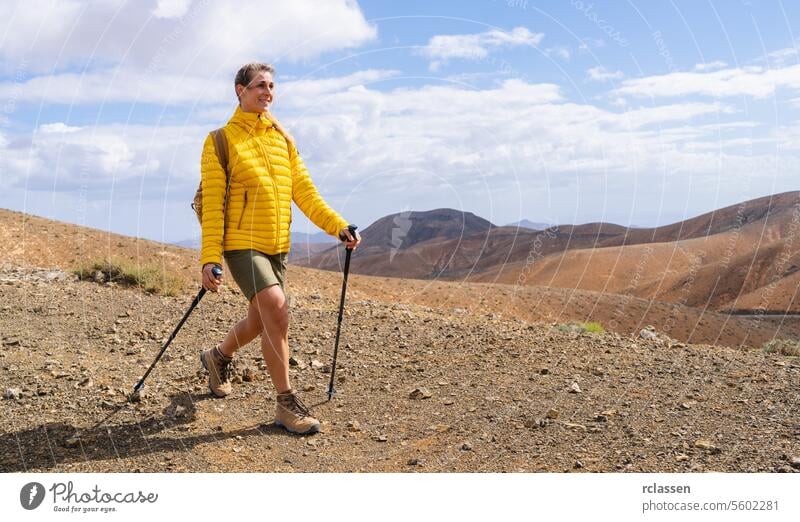 Lächelnder Wanderer in gelber Jacke mit Trekkingstöcken in bergigem Wüstengelände Fuerteventura gelbe Jacke wüst Berge Outdoor-Erlebnis wandern Nachlauf Natur