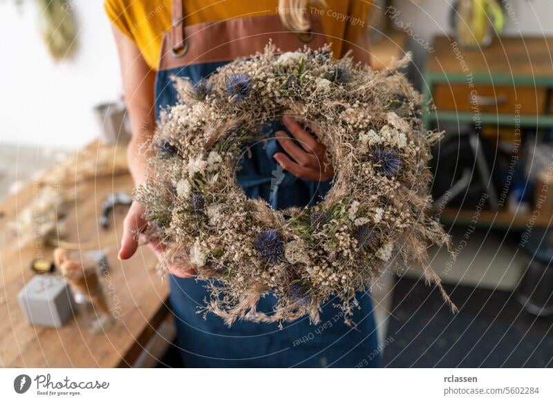 Florist präsentiert einen fast fertigen Trockenblumenkranz, der seine Texturen und Farben zur Geltung bringt Blumenhändler Kranz aus Trockenblumen Werkstatt