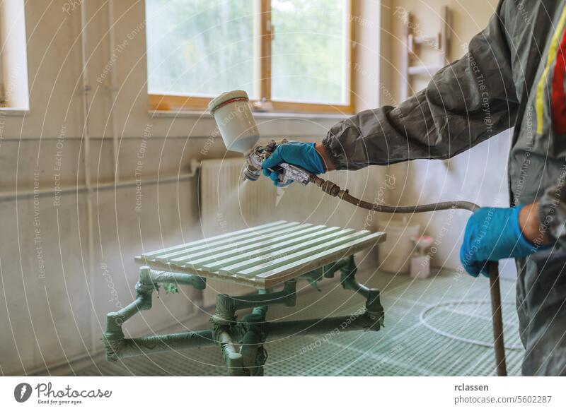 Eine Person in einem Schutzanzug besprüht eine Holzplatte in einer Schreinerei Zimmerer Kunsthandwerker Mundschutz Farbe Spritzpistole Anstreicher Werkstatt