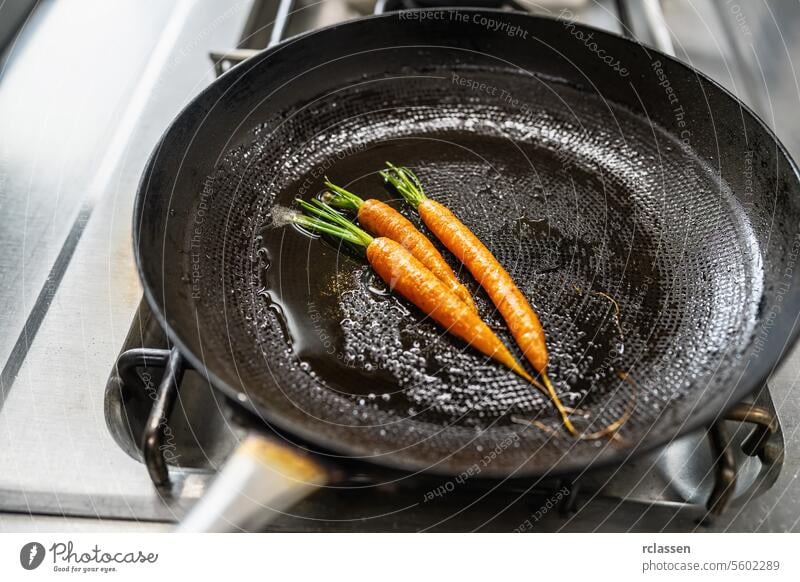 Karotten braten in geölten Pfanne auf einem Gasherd in einer professionellen Küche in einem Restaurant. Luxus-Hotel Kochen Konzept Bild. Gemüse Sautieren