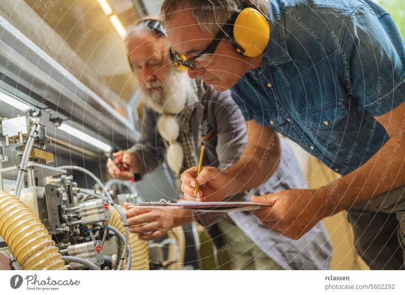 Zwei Männer mit Gehörschutz bei der Arbeit an Maschinen in einer Holzwerkstatt Ohrenschützer arbeiten Techniker industriell Schreinerei Einstellung Teamwork