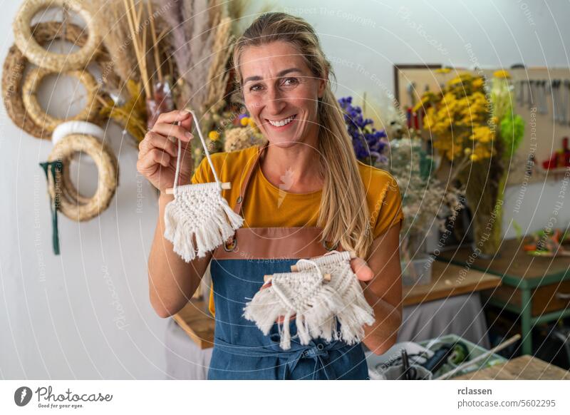 Blumenhändlerin präsentiert in ihrem Geschäft handgefertigte Makramee-Pflanzenbügel Vorstellung von Werkstatt Frau Lächeln Handwerk Dekoration & Verzierung diy