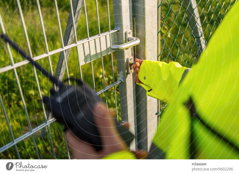 Sicherheitspersonal, das mit einem Walkie-Talkie in der Hand ein Tor entriegelt freischalten Gate Funkgerät Taste Mitteilung Metalltor Schloss sicheres Zugang