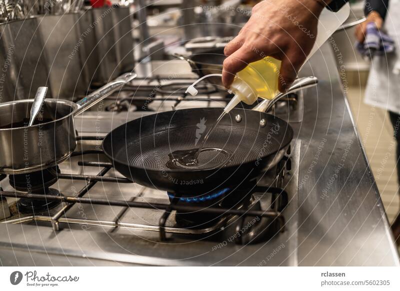 Chefkoch gießt Öl in eine beheizte Pfanne. Luxushotel Kochen Konzept Bild. Hand Küche Hotel Küchenchef Ölgießen Profiküche Essen zubereiten Herdplatte