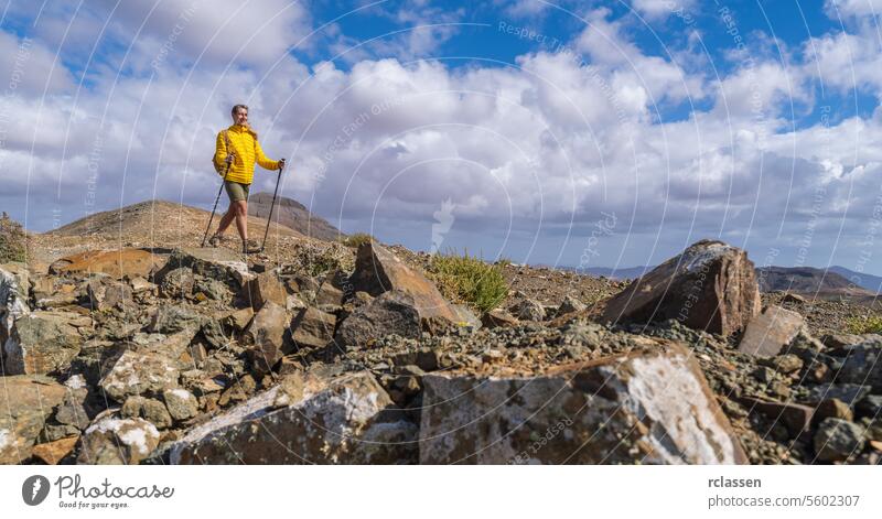 Wanderer in Gelb auf felsigem Berggelände mit bewölktem blauem Himmel im Hintergrund Fuerteventura gelbe Jacke Wolken Blauer Himmel Outdoor-Erlebnis wandern