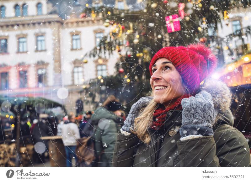 Fröhliche Frau mit roter Mütze, die auf einem Weihnachtsmarkt in den fallenden Schnee schaut, mit Platz für Ihren individuellen Text. Frohe Weihnachten Kakao