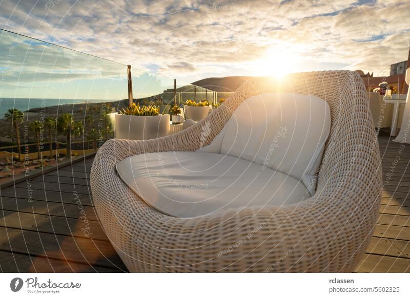 Liegestuhl aus Korbgeflecht auf einer Hotelterrasse bei Sonnenuntergang mit Blick auf das Meer und die Berge Loungesessel Meerblick Bergblick Schiffsdeck