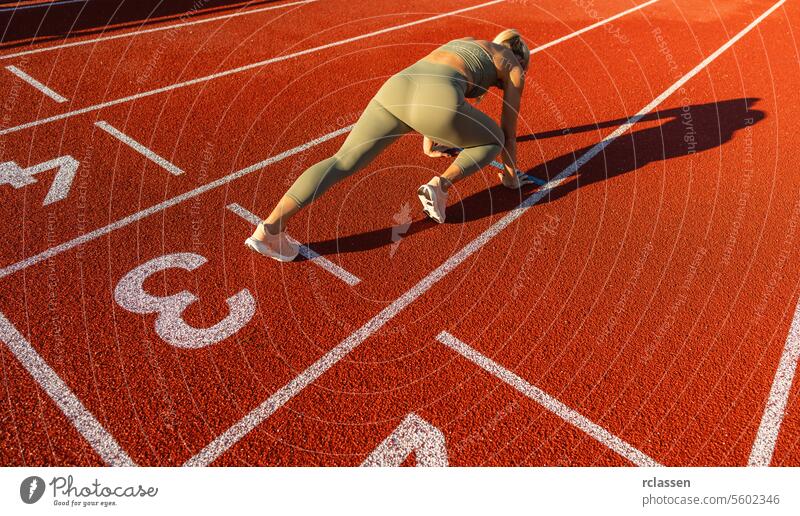 Läufer in Startposition auf einer roten Bahn, Sonnenlicht wirft Schatten, Sportkleidung, Fitness Athlet Startblock Rennen Leichtathletik Sprinter Konkurrenz