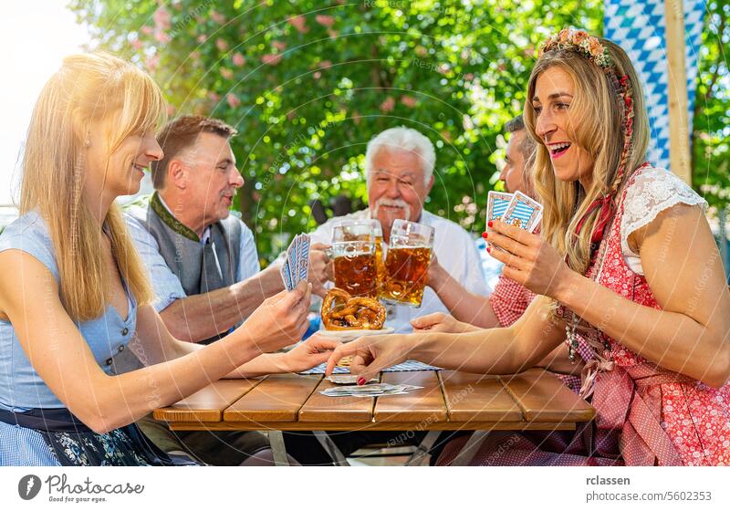 Bayern in Tracht beim Kartenspielen im Biergarten oder auf dem Oktoberfest Glücksspiel Spielen Blockwart anfeuern Brezeln Freunde Frau Großvater Senior Fahne