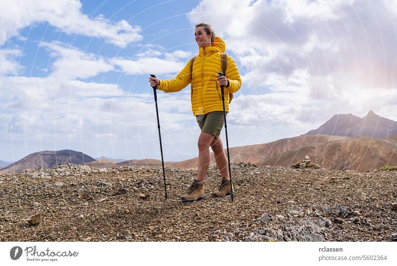 Wanderer in gelber Jacke mit Trekkingstöcken auf einem felsigen Bergpfad, Berge im Hintergrund Fuerteventura gelbe Jacke Bergweg wandern im Freien Abenteuer