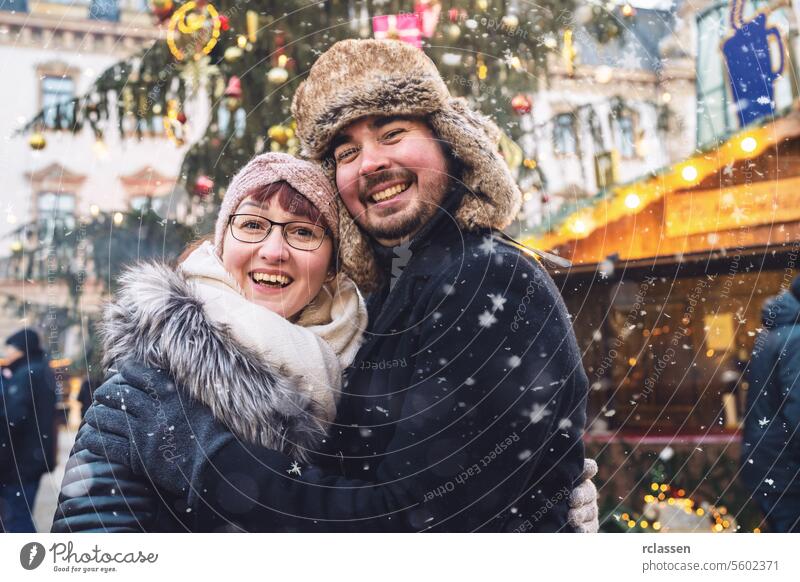 Glückliches Paar, das sich auf einem verschneiten Weihnachtsmarkt umarmt und freudig lächelt Freunde Glühwein Vollbart Tourismus Datierung Fairness reisen Liebe