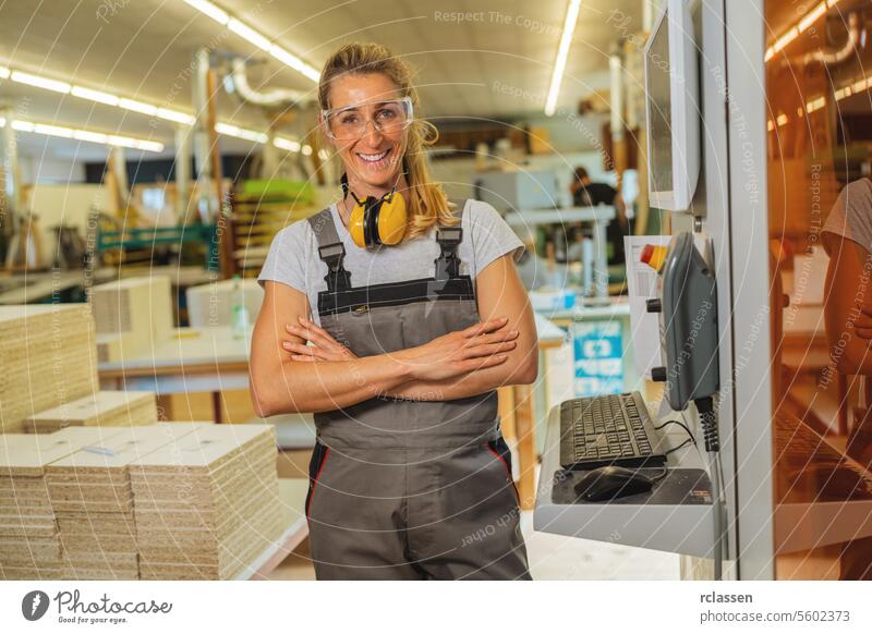 Selbstbewusste Frau mit verschränkten Armen und Gehörschutz in einer Tischlerwerkstatt professioneller Handwerker Möbelindustrie Arbeiter Schnittholz