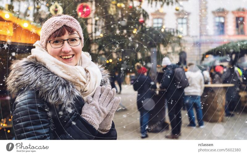 Junge Frau auf einem verschneiten Weihnachtsmarkt, in Winterkleidung und mit Mütze, lächelt in die Kamera, mit Platz für Ihren individuellen Text. Tourist
