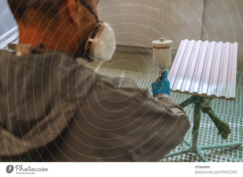 Person in Schutzkleidung beim Spritzen einer Holzplatte mit einem Fenster im Hintergrund Zimmerer Kunsthandwerker Mundschutz Farbe Spritzpistole Anstreicher