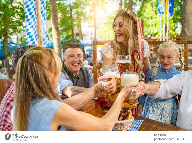 Freunde und Familie in Tracht, Dirndl und Lederhosen sitzen vergnügt am Tisch, trinken Bier und essen Brezeln im Biergarten oder beim Oktoberfest in Bayern, Deutschland