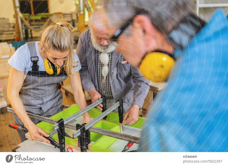 Drei Schreiner mit Gehörschutz bei der Arbeit an einem eingespannten Holzstück in einer Werkstatt Teamwork professionell Kunsthandwerker Hobelbank