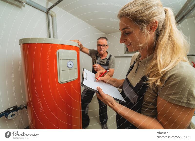 Ein Team von Heizungsmonteuren überprüft eine alte Gasheizung und hält ein Klemmbrett mit einer Checkliste in einem Heizungsraum in einem Haus. Gasheizung Ersatz Verpflichtung Konzept Bild