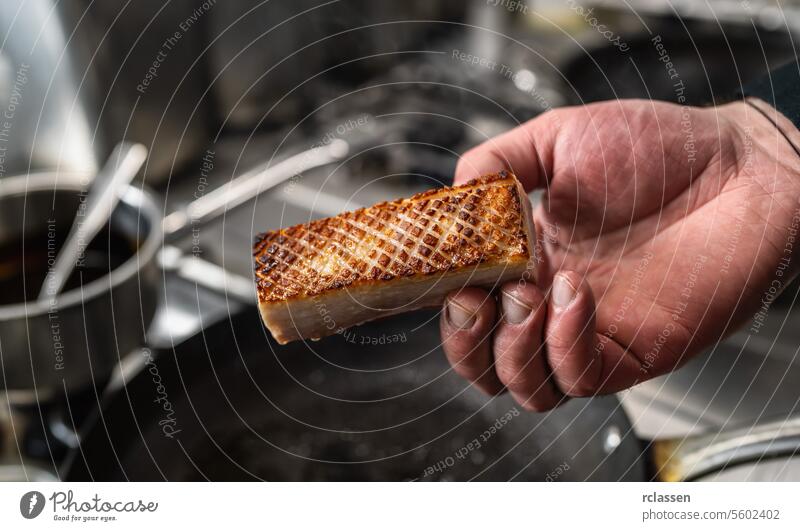 Hand hält einen knusprigen Schweinebauch, der in einer heißen Pfanne in einer professionellen Küche in einem Restaurant gebraten wurde. Luxus-Hotel Kochen Konzept Bild.