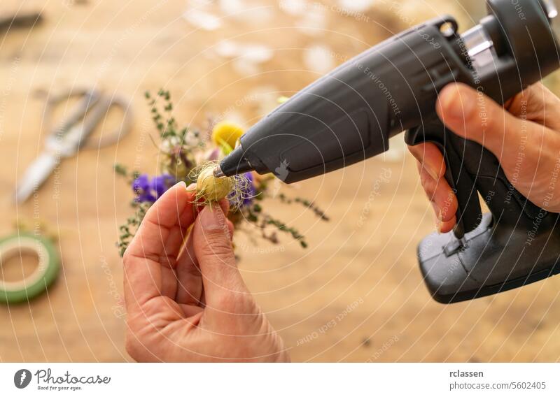 Hände, die eine Klebepistole für ein kleines Blumenprojekt benutzen Leimpistole Blumenhandwerk diy handgefertigt Projekt Handwerkszeug Kreativität Heißkleber